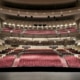 Wide view of a large, modern theater auditorium with multiple balconies and rows of red seats, seen from the stage looking out toward the house.