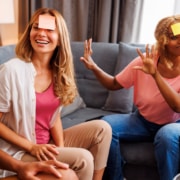 Group of friends sitting together on a couch, actively gesturing and laughing while playing charades indoors.