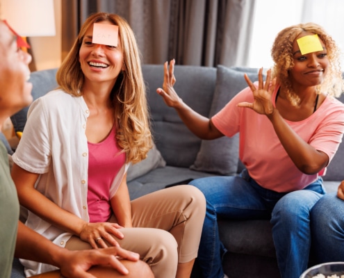 Group of friends sitting together on a couch, actively gesturing and laughing while playing charades indoors.