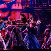 A large dance company in street clothes dance on stage