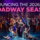 Colorful theatrical cast performing a lively dance number on a grand, art‑deco–inspired stage, with bold text above reading ‘Announcing the 2026/2027 Broadway Season.’ Bright costumes, dramatic lighting, and ornate set pieces create an energetic Broadway atmosphere.