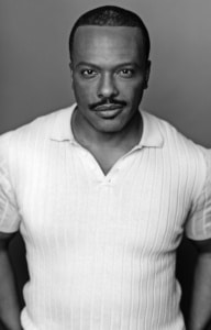 Black‑and‑white studio portrait of a person wearing a textured white polo shirt against a plain background.