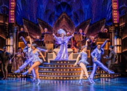 A lavish stage production with 4 dancers, 1 singer, onstage musicians and several actors in military attire looking on.