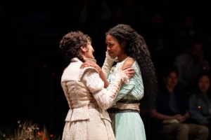 Two performers face each other closely and hold one another by the shoulders during an intimate moment onstage.