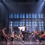 Cast performing a high‑energy dance number in vibrant purple costumes on stage in the MJ musical touring production.