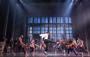 Cast performing a high‑energy dance number in vibrant purple costumes on stage in the MJ musical touring production.