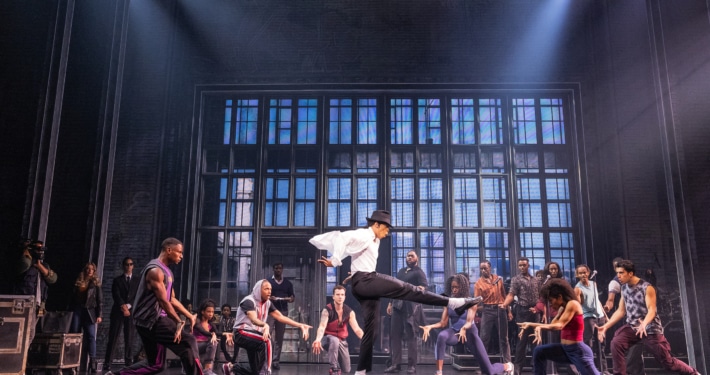 Cast performing a high‑energy dance number in vibrant purple costumes on stage in the MJ musical touring production.