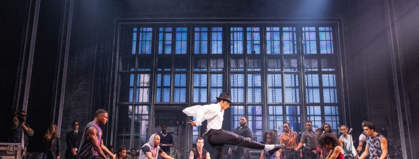 Cast performing a high‑energy dance number in vibrant purple costumes on stage in the MJ musical touring production.