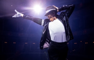 MJ musical performer striking an iconic dance pose under dramatic spotlight wearing a fedora, sequin jacket, and white glove.