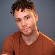 Person wearing an orange shirt with short curly hair in a studio portrait”
