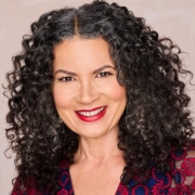 Person with voluminous curly hair wearing a patterned top in a studio portrait