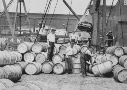 Early 20th‑century dock workers handling barrels during waterfront shipping operations