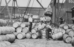 Early 20th‑century dock workers handling barrels during waterfront shipping operations