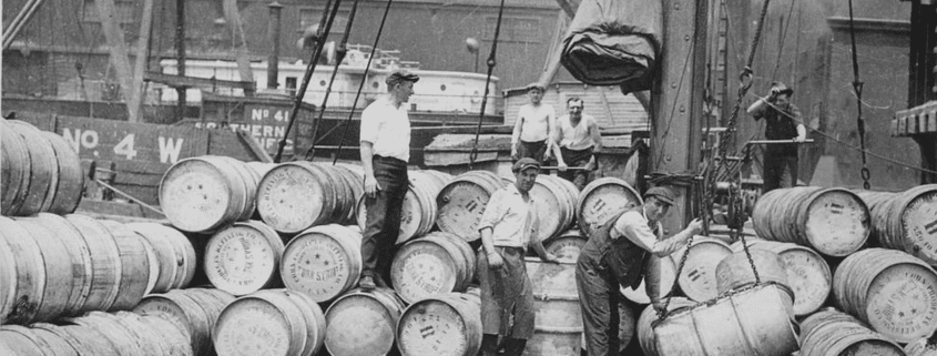 Early 20th‑century dock workers handling barrels during waterfront shipping operations