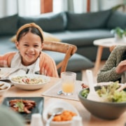A dining table set with various dishes while two children sit and eat, with an older person seated in the foreground in a home living room setting.
