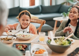 A dining table set with various dishes while two children sit and eat, with an older person seated in the foreground in a home living room setting.