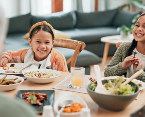 A dining table set with various dishes while two children sit and eat, with an older person seated in the foreground in a home living room setting.