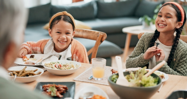 A dining table set with various dishes while two children sit and eat, with an older person seated in the foreground in a home living room setting.