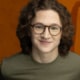 Studio headshot of person wearing glasses with curly hair against orange background