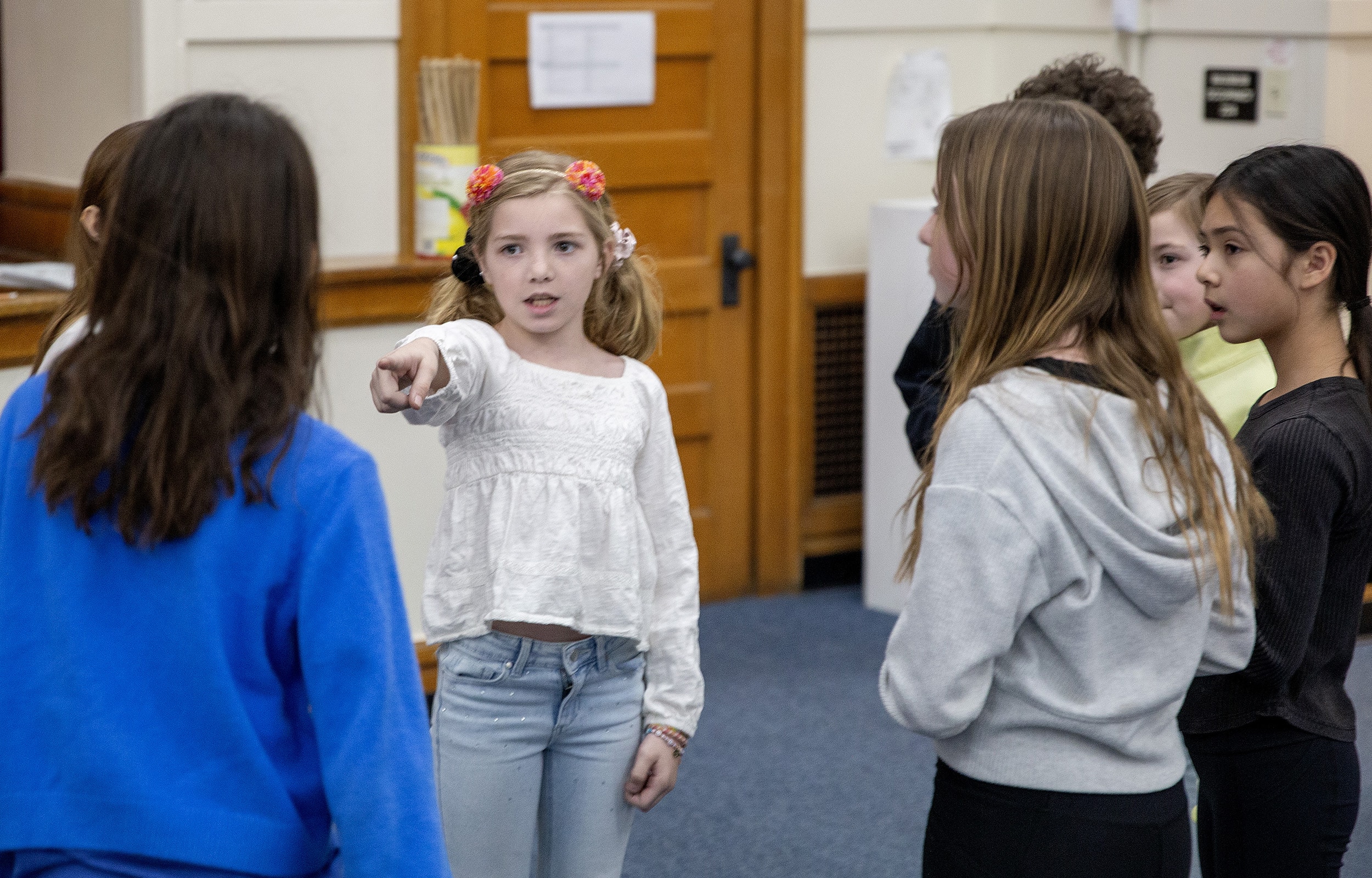 A student points toward another student while participating in a theater exercise, as a small group stands in a school auditorium.