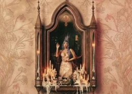 Ornate artwork showing a central framed niche with a crowned, seated figure surrounded by lit candles, set against a decorative beige patterned background.
