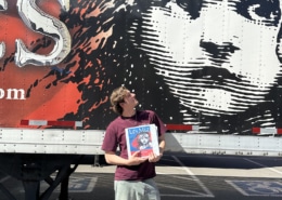 Person holding a Les Misérables booklet while standing in front of a large truck mural featuring the iconic Cosette illustration and red-and-black show artwork.