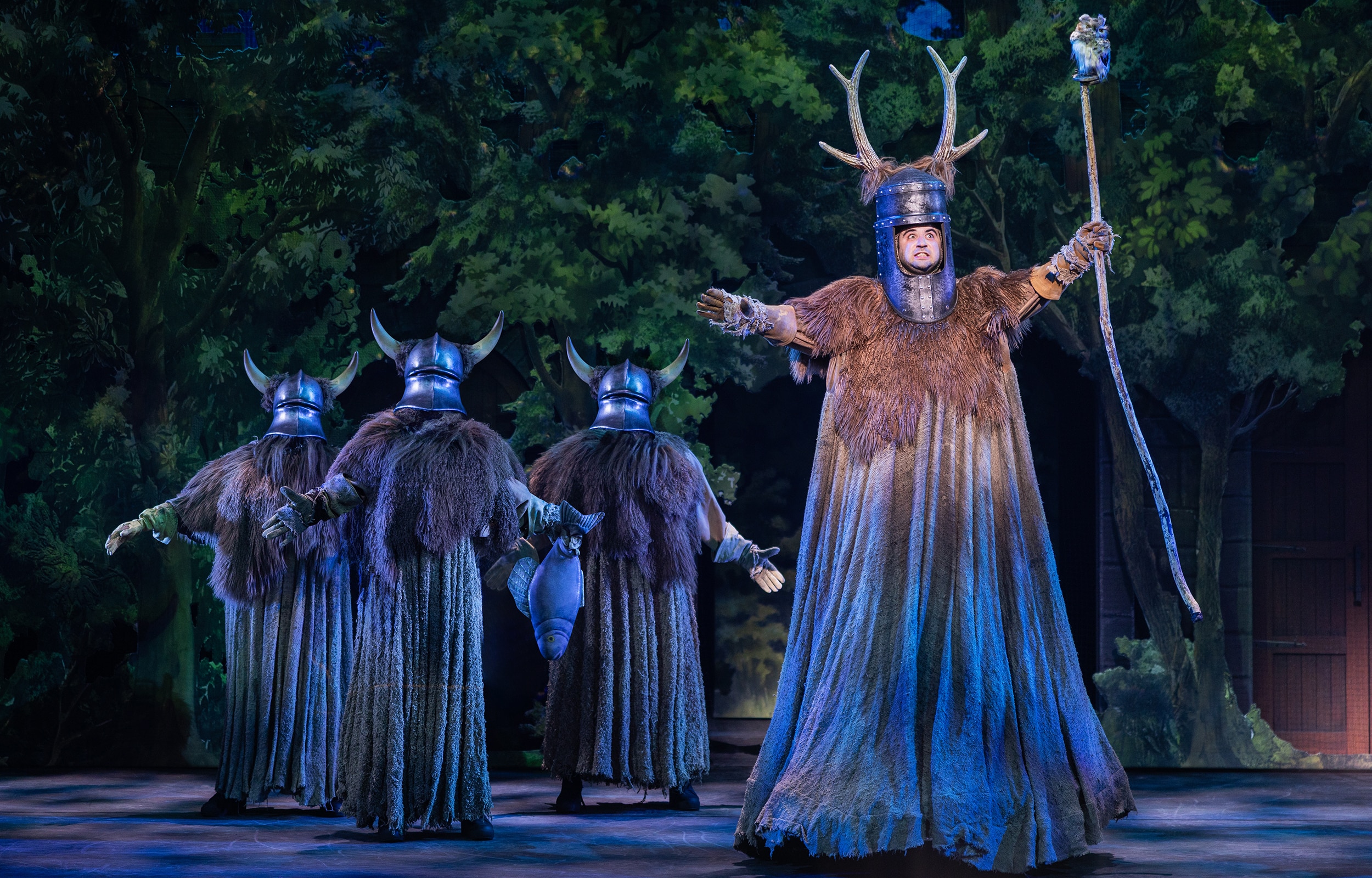 Spamalot stage production with antlered knight and ensemble performing in a forest setting