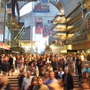Large crowd of people moving through a busy indoor atrium at the Denver Performing Arts Complex, with theater signage and balconies visible above.