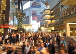 Large crowd of people moving through a busy indoor atrium at the Denver Performing Arts Complex, with theater signage and balconies visible above.
