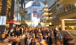 Large crowd of people moving through a busy indoor atrium at the Denver Performing Arts Complex, with theater signage and balconies visible above.