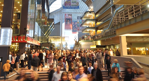 Large crowd of people moving through a busy indoor atrium at the Denver Performing Arts Complex, with theater signage and balconies visible above.