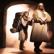 Medieval comedy scene from Monty Python’s Spamalot musical featuring knights and a traveler entering a castle