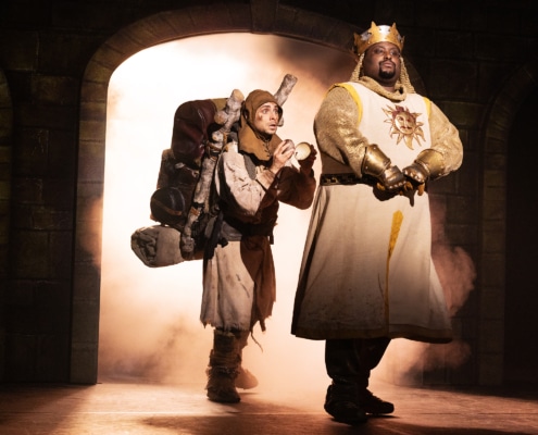 Medieval comedy scene from Monty Python’s Spamalot musical featuring knights and a traveler entering a castle