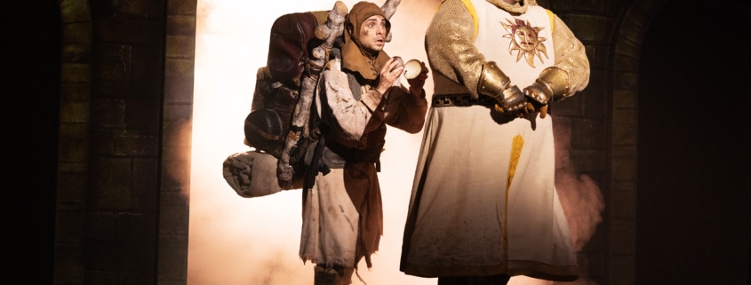 Medieval comedy scene from Monty Python’s Spamalot musical featuring knights and a traveler entering a castle
