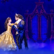 Belle and the Beast dance beneath a moonlit sky in Disney's Beauty and the Beast, surrounded by a romantic castle backdrop and theatrical fog.