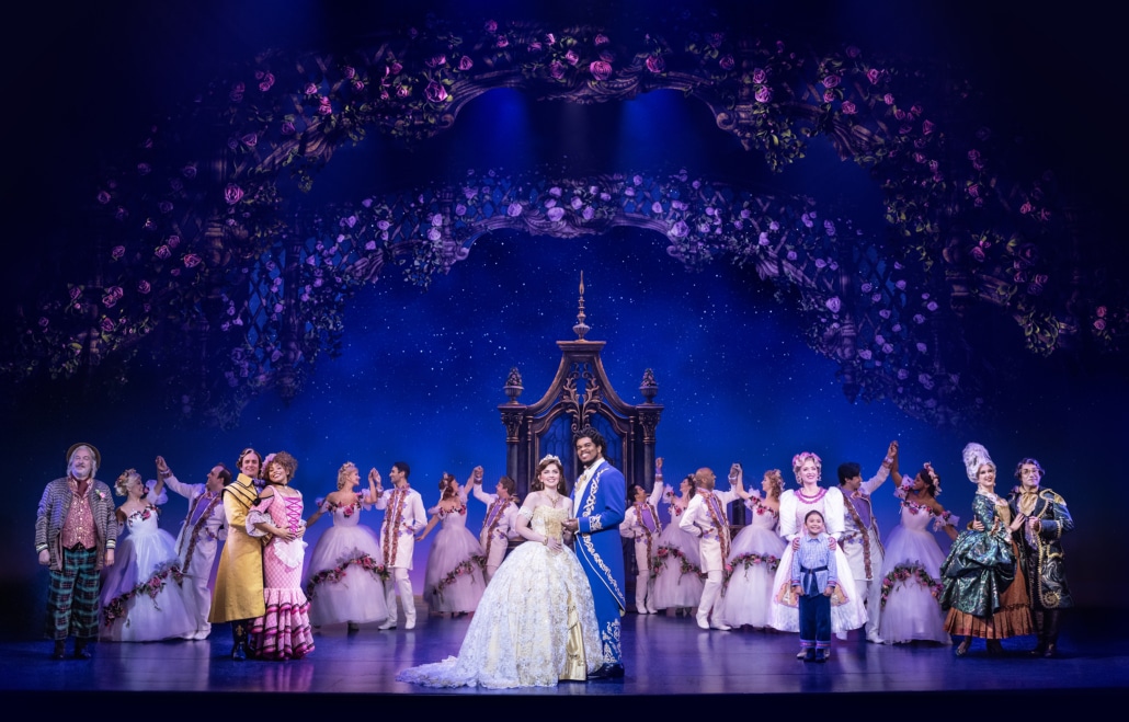 The cast of Disney's Beauty and the Beast performs a grand finale beneath a floral arch, with Belle and the Beast center stage in an elaborate fairytale setting.