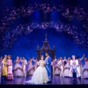 The cast of Disney's Beauty and the Beast performs a grand finale beneath a floral arch, with Belle and the Beast center stage in an elaborate fairytale setting.