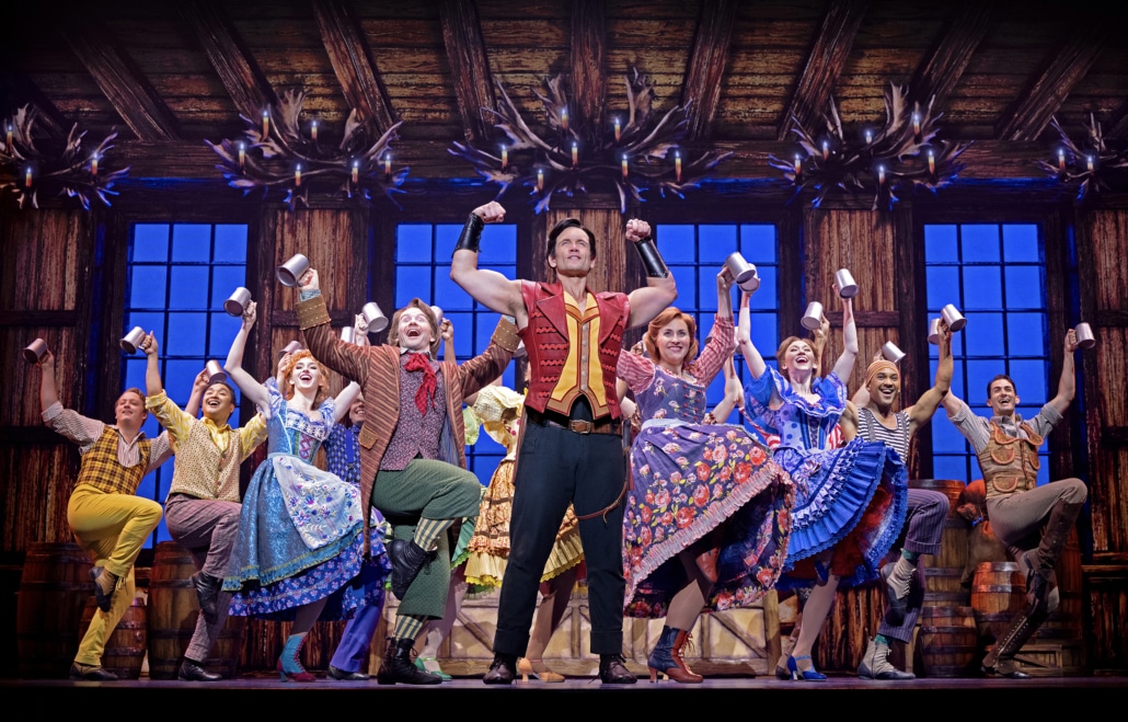 Cast members perform the lively Gaston tavern scene in Disney's Beauty and the Beast, featuring colorful costumes, tankards, and a rustic inn set.