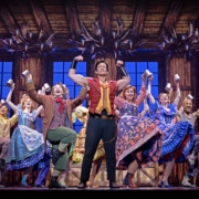 Cast members perform the lively Gaston tavern scene in Disney's Beauty and the Beast, featuring colorful costumes, tankards, and a rustic inn set.