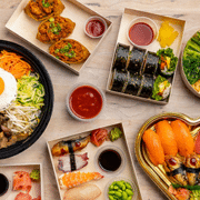 Assorted Asian-inspired dishes from OGO Kitchen at Denver Union Station, including bibimbap, sushi rolls, salmon poke bowl, dumplings, and fresh sashimi platters.