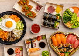 Assorted Asian-inspired dishes from OGO Kitchen at Denver Union Station, including bibimbap, sushi rolls, salmon poke bowl, dumplings, and fresh sashimi platters.