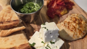 Mediterranean appetizer board at Olive & Finch Golden Triangle featuring pita bread, feta cheese, hummus, olives, roasted vegetables, and herb pesto.