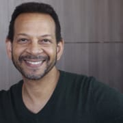 Professional headshot of a person with short hair and a neatly trimmed beard wearing a dark V-neck sweater. The portrait is framed from the chest up against a neutral indoor background with soft natural lighting.