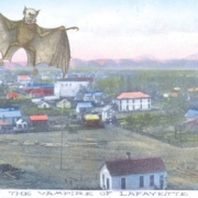 Vintage postcard-style illustration showing a winged bat-like creature with a human face flying over a small town. The image includes the caption “The Vampire of Lafayette” along the bottom.