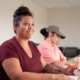 A participant seated at a classroom table during a training session, with another participant taking notes in the background.