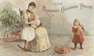 Victorian Christmas card titled “Using Mamma’s Christmas Present.” A seated figure in a rocking chair cradles a doll, while a child in a red dress pulls a toy wagon carrying a doll. Additional toys, including a tricycle, hobby horse, and small wagon, appear in the background of a softly colored holiday scene.