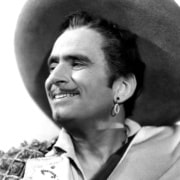 Black-and-white close-up portrait of a person wearing a wide-brimmed hat, an earring, and a costume jacket, photographed in profile while looking off to the side.