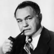Black-and-white studio portrait of a person in a dark suit and patterned tie holding a tobacco pipe, posed against a plain background.