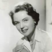 Black-and-white studio portrait of a person wearing a light-colored blouse and pearl necklace, seated and facing the camera against a softly lit background.