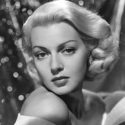 Black-and-white glamour portrait of a person with short, carefully styled hair, posed with one shoulder exposed against a softly illuminated background.